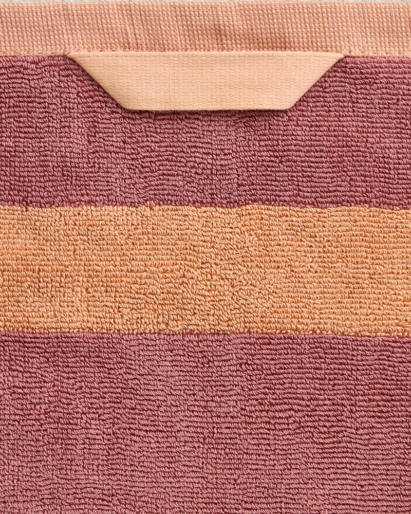 A detailed view of the Bed Threads Terracotta & Pink Clay Two-Toned 100% Cotton Terry Bath Sheet features a horizontal pink stripe on terracotta, a folded hanging loop, and a quick-drying design.