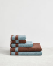 The Bed Threads Cacao & Lagoon Two-Toned 100% Cotton Terry Bath Sheet Bundle features four plush bath towels, neatly stacked from largest to smallest, in alternating blue and brown, displayed on a plain white background. - view