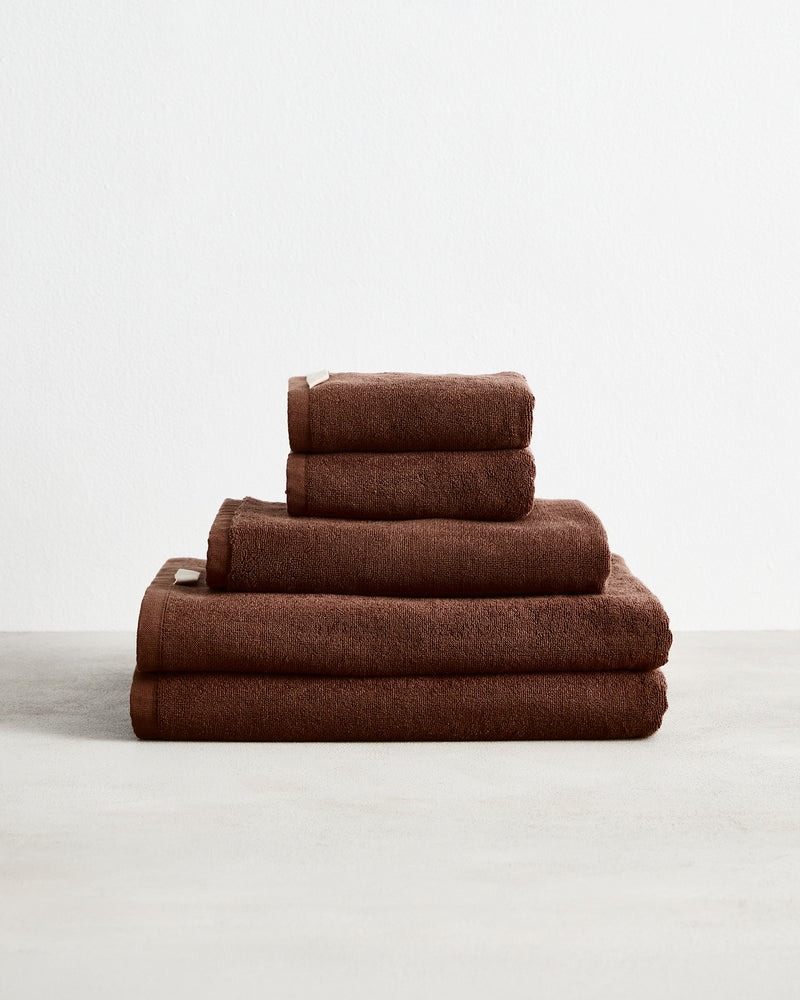 The Bed Threads Espresso 100% Cotton Terry Bath Sheet Bundle features neatly stacked, highly absorbent brown towels in multiple sizes, arranged on a light surface with a plain white background.