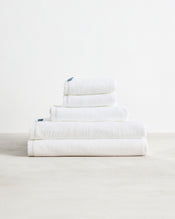 The Bed Threads Crisp White 100% Cotton Terry Bath Sheet Bundle features highly absorbent towels in various sizes, neatly stacked on a light surface against a plain white background. - view