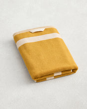 A Crème & Turmeric Two-Toned 100% Cotton Terry Bath Towel by Bed Threads, featuring thick white stripes, is neatly folded on a light textured surface. - view
