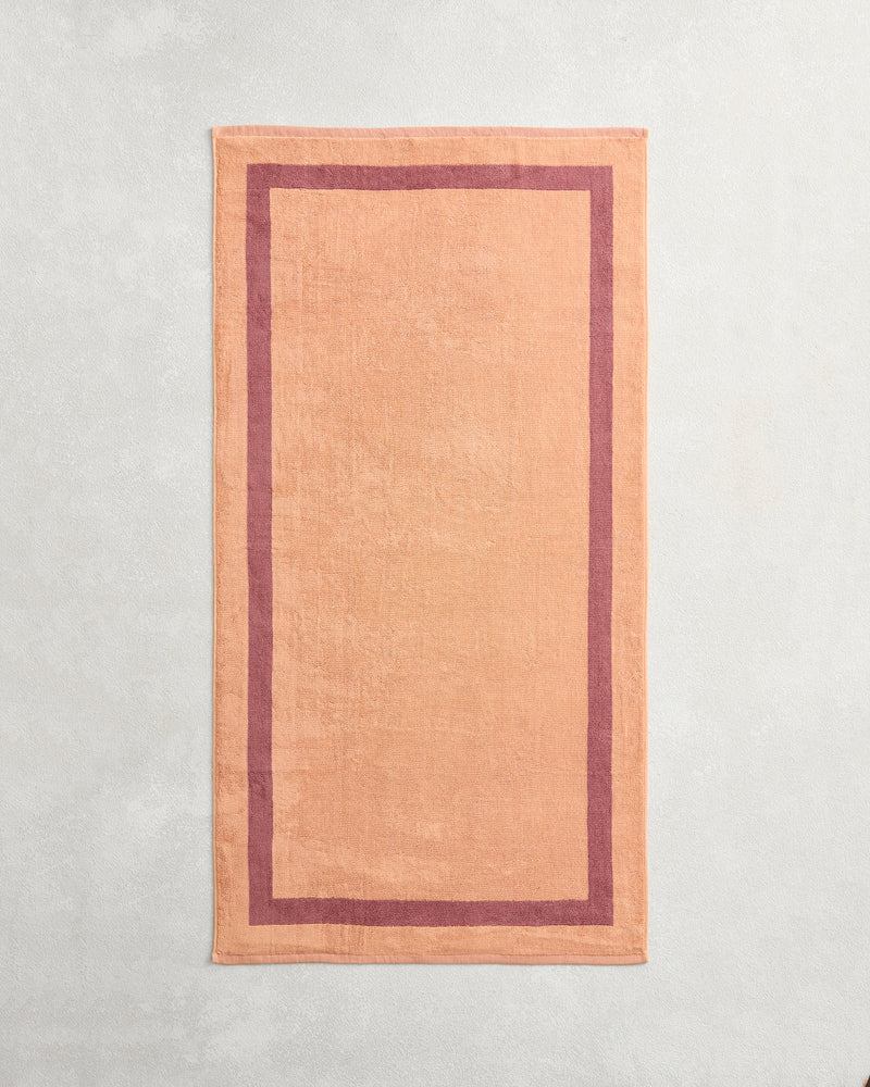 A terracotta and pink clay two-toned 100% cotton terry bath towel from Bed Threads is laid flat on a lightly textured surface.