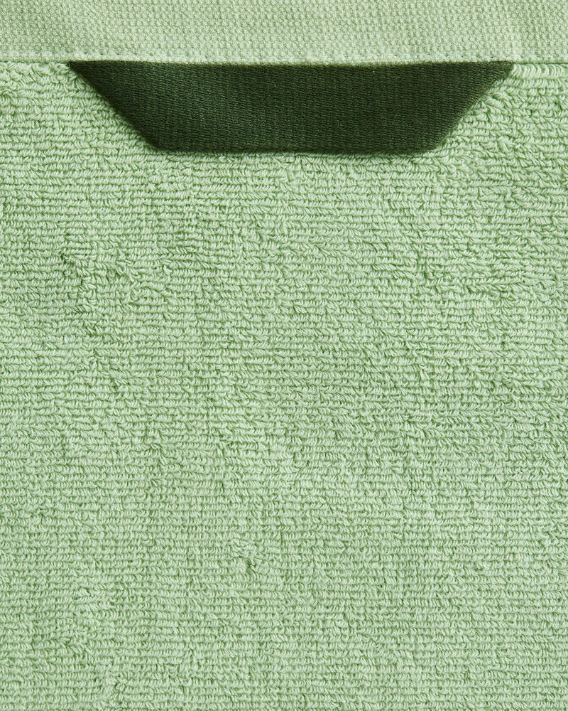 Close-up of Bed Threads' Apple 100% Cotton Terry Bath Towels (Set of Two), featuring a light green, textured looped surface and dark green hanging loop, showcasing their highly absorbent cotton quality.