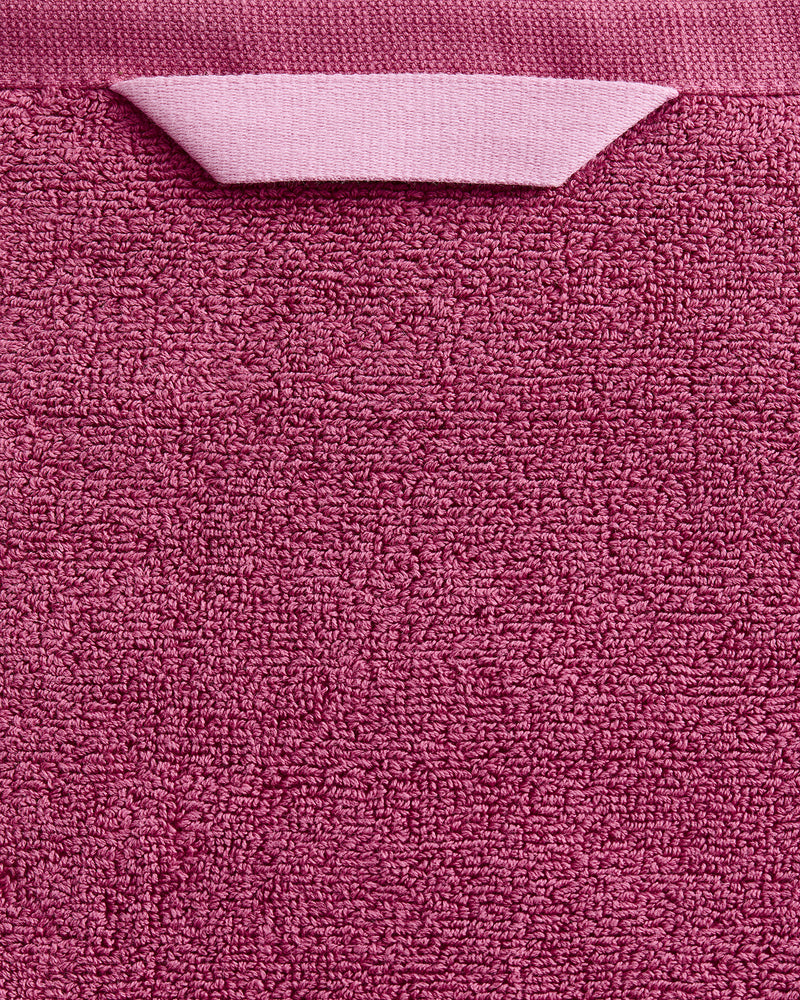 A close-up of the Bed Threads Berry 100% Cotton Terry Bath Towel shows its textured, plush pink fabric and a matching hanging loop at the top.