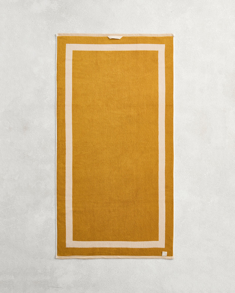 The Bed Threads Crème & Turmeric Two-Toned 100% Cotton Terry Bath Towel, 650GSM, is laid flat to highlight its plush texture and elegant beige border.