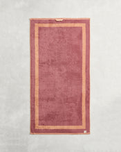 The Bed Threads Terracotta & Pink Clay Two-Toned 100% Cotton Terry Bath Towel Bundle features rectangular bath towels in rose and light pink, with a subtle border and beige tag, displayed flat on a light, textured surface. - view