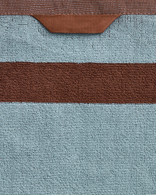 A close-up of Bed Threads' Cacao & Lagoon Two-Toned 100% Cotton Terry Bath Towels (Set of Two), featuring a wide horizontal brown stripe on a light blue background and a brown hanging loop at the top edge.
