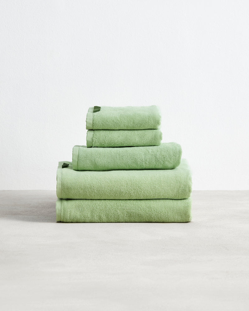 A neatly stacked Bed Threads Apple 100% Cotton Terry Bath Towel Bundle of four light green, highly absorbent towels in varying sizes, arranged largest to smallest, set against a plain white background.