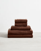 The Bed Threads Espresso 100% Cotton Terry Bath Towel Bundle, featuring neatly stacked towels in various sizes, is displayed on a light surface against a plain white background. - view