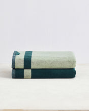The Bed Threads Forest & Sage Two-Toned 100% Cotton Terry Bath Towels (Set of Two) are neatly folded and stacked on a light beige surface with a plain white background. - view