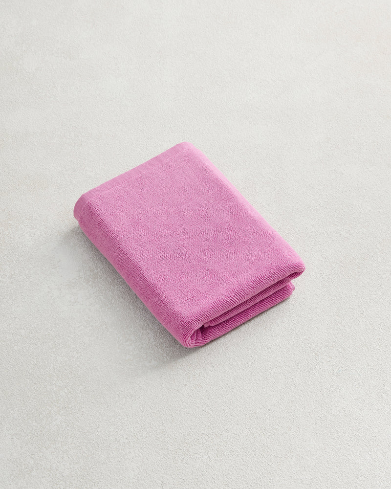 A Bubblegum 100% Cotton Terry Bath Mat by Bed Threads is displayed on a light, textured surface with a neatly folded pink towel beside it.