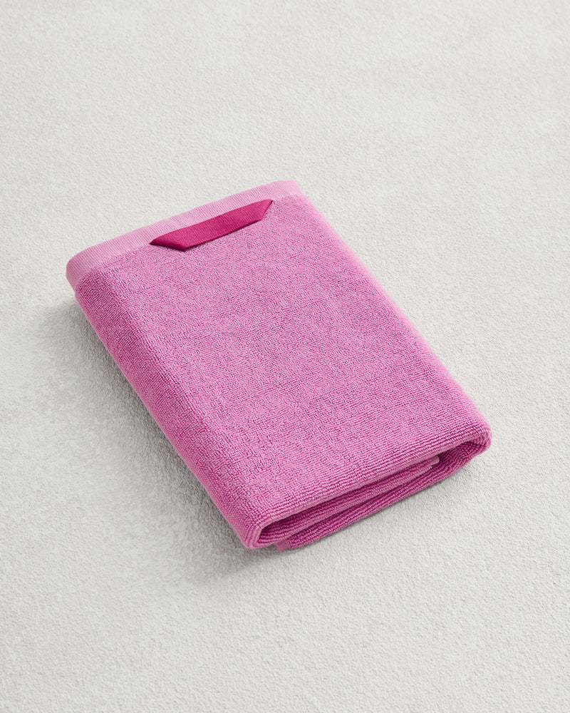 The Bed Threads Bubblegum 100% Cotton Terry Hand Towel, featuring plush 650GSM fabric, is neatly folded on a light textured surface, highlighting its ultimate softness, quick-drying convenience, and small fabric tag.