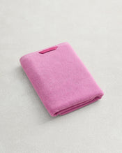 The Bed Threads Bubblegum 100% Cotton Terry Bath Towel, featuring a small rectangular tag and quick-drying 650GSM terry fabric, is folded on a light textured surface. - view
