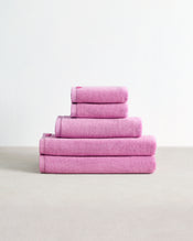 A set of four folded Bubblegum 100% Cotton Terry Bath Towels from Bed Threads rests neatly on a light beige surface against a plain white background. - view