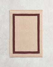 Flat cotton terry bath mat on a grey background in a creme colour with a cacao border. - view