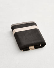 A folded cotton terry bath mat on a grey background, in a charcoal colourway with an oatmeal border.  - view