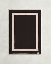 Flat cotton terry bath mat on a grey background in a charcoal colour with an oatmeal border. - view