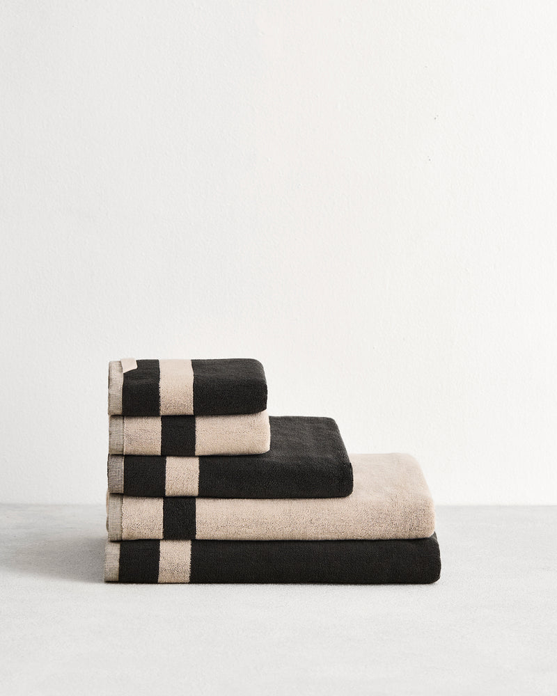 Stack of cotton terry bath towels in reversible colours oatmeal and charcoal.