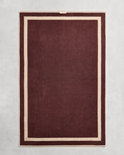 Flat cotton terry bath sheet on a grey background in a cacao colour with a creme border. - view