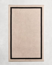 Flat cotton terry bath sheet on a grey background in an oatmeal colour with a charcoal border. - view
