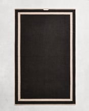 Flat cotton terry bath sheet on a grey background in a charcoal colour with an oatmeal border. - view