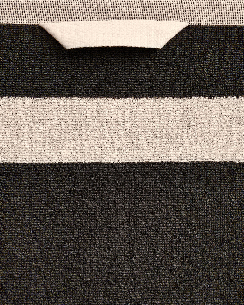 Close-up of a cotton terry bath towel in a charcoal colourway with an oatmeal border.