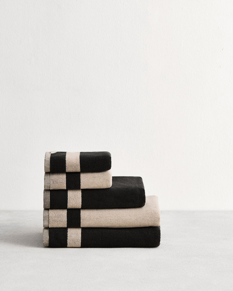 Stack of cotton terry bath towels in reversible colours oatmeal and charcoal.