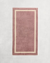 Flat cotton terry towel on a grey background in a lavender colour with a creme border. - view