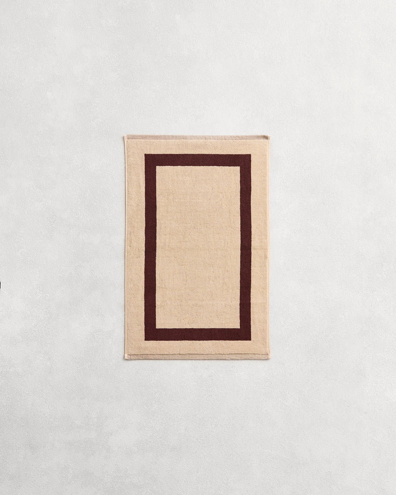 Flat cotton terry hand towel on a grey background in a creme colour with a cacao border.