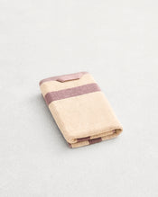 A folded cotton terry hand towel on a grey background, in a creme colourway with a lavender border.  - view