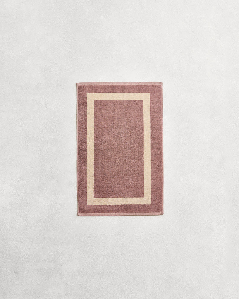 Flat cotton terry hand towel on a grey background in a lavender colour with a creme border.