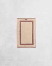 Flat cotton terry hand towel on a grey background in a creme colour with a lavender border. - view