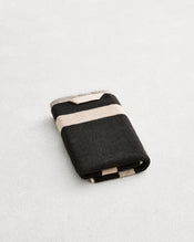 A folded cotton terry hand towel on a grey background, in a charcoal colourway with an oatmeal border.  - view