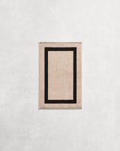 Flat cotton terry hand towel on a grey background in an oatmeal colour with a charcoal border. - view