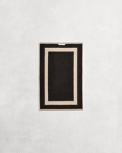 Flat cotton terry hand towel on a grey background in a charcoal colour with an oatmeal border. - view