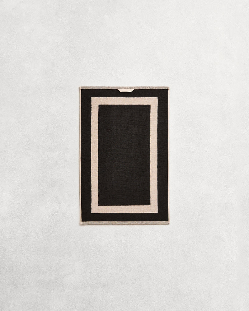 Flat cotton terry hand towel on a grey background in a charcoal colour with an oatmeal border.