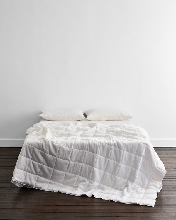 A neatly made bed with two pillows and the white, machine-washable Does-It-All Duvet Insert by Bed Threads sits against a plain white wall on a dark wooden floor.