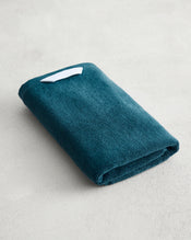 The Bed Threads Aegean 100% Cotton Terry Hand Towel, featuring plush 650GSM terry and a small white tag, is neatly folded on a light gray textured surface. - view