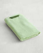 The Apple 100% Cotton Terry Hand Towel by Bed Threads, in light green, is neatly folded on a light gray textured surface, highlighting its plush 650GSM fabric for superior comfort. - view