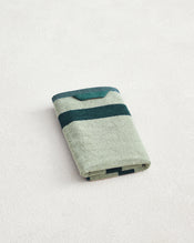 A Forest & Sage Two-Toned 100% Cotton Terry Hand Towel by Bed Threads, featuring dark green horizontal stripes and plush 650GSM terry, is neatly folded on a light textured surface to showcase its ultimate softness. - view