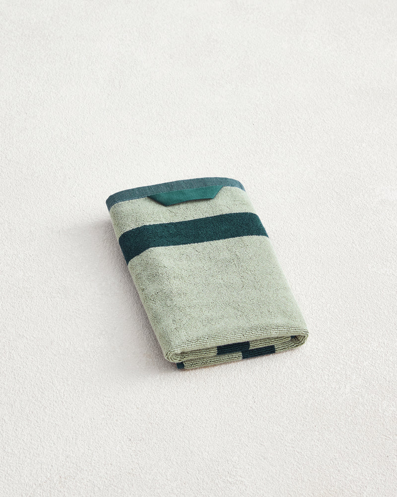 A Forest & Sage Two-Toned 100% Cotton Terry Hand Towel by Bed Threads, featuring dark green horizontal stripes and plush 650GSM terry, is neatly folded on a light textured surface to showcase its ultimate softness.