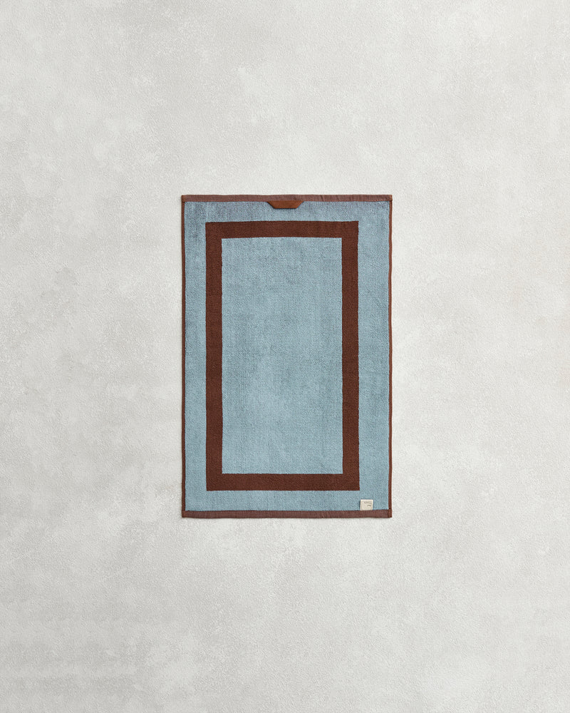 The Cacao & Lagoon Two-Toned 100% Cotton Terry Hand Towel from Bed Threads features a rectangular blue design with a dark brown border and matching inner outline, displayed on a light textured background.