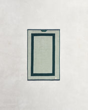 The Bed Threads Forest & Sage Two-Toned 100% Cotton Terry Hand Towels (Set of Two) feature two dark green borders on a light gray background, displayed flat on a textured off-white surface. - view