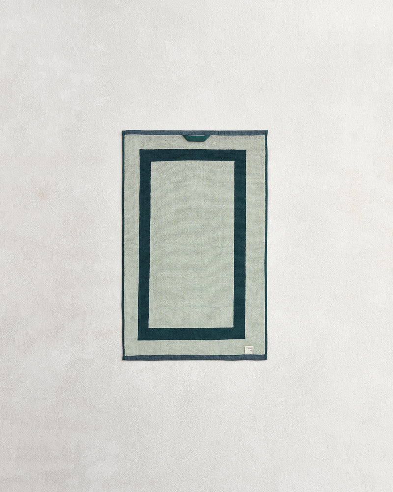 The Bed Threads Forest & Sage Two-Toned 100% Cotton Terry Hand Towels (Set of Two) feature two dark green borders on a light gray background, displayed flat on a textured off-white surface.