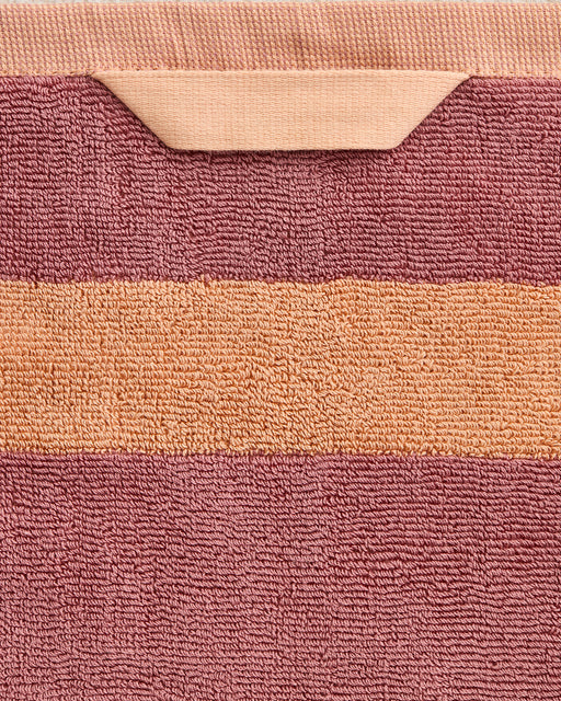 A close-up of the Bed Threads Terracotta & Pink Clay Two-Toned 100% Cotton Terry Hand Towel, showing a peach stripe and matching loop, set against muted mauve terry fabric.