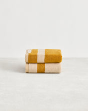 The Crème & Turmeric Two-Toned 100% Cotton Terry Hand Towels (Set of Two) by Bed Threads are plush 650GSM, quick-drying, and feature mustard and cream stripes, neatly folded on a white background for a stylish touch. - view