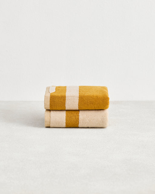 The Crème & Turmeric Two-Toned 100% Cotton Terry Hand Towels (Set of Two) by Bed Threads are plush 650GSM, quick-drying, and feature mustard and cream stripes, neatly folded on a white background for a stylish touch.