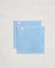 A set of two Sky 100% Cotton Terry Face Washers by Bed Threads, in light blue with small beige labels, are slightly overlapping on a textured surface—ideal for your daily skincare routine. - view