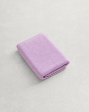 The Bed Threads Violet 100% Cotton Terry Bath Mat, in a soft lavender shade, sits on a light textured surface next to a neatly folded matching towel for ultimate comfort and luxury. - view