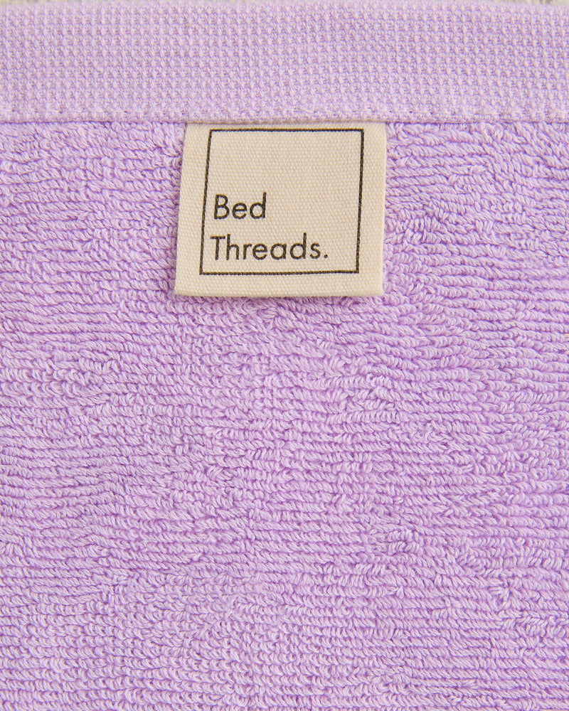 A close-up of Violet 100% Cotton Terry Face Washers (Set of Two) by Bed Threads, featuring a fabric label sewn near the edge—absorbent, gentle on the skin, and perfect for daily cleansing.